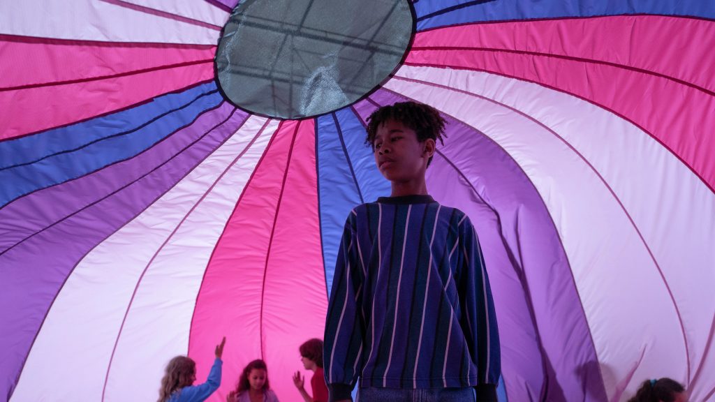 Ian Foreman en una escena de la película. Al fondo, se puede ver cómo la tela muestra los colores de la bandera trans.